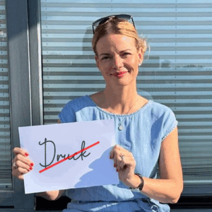 Bild von Christiane Witt mit einem A4 Blatt in Händen auf dem das Wort DRUCK steht und durchgestrichen wurde